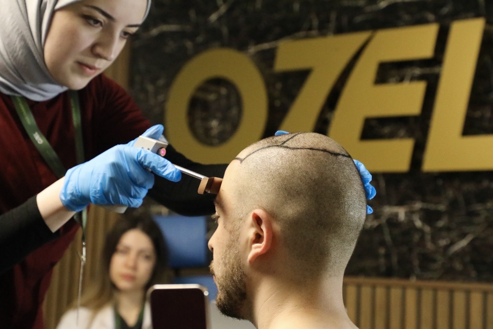 An OZEL specialist drawing a patient’s hairline with a measuring tool, in front of the OZEL logo at the clinic in Istanbul