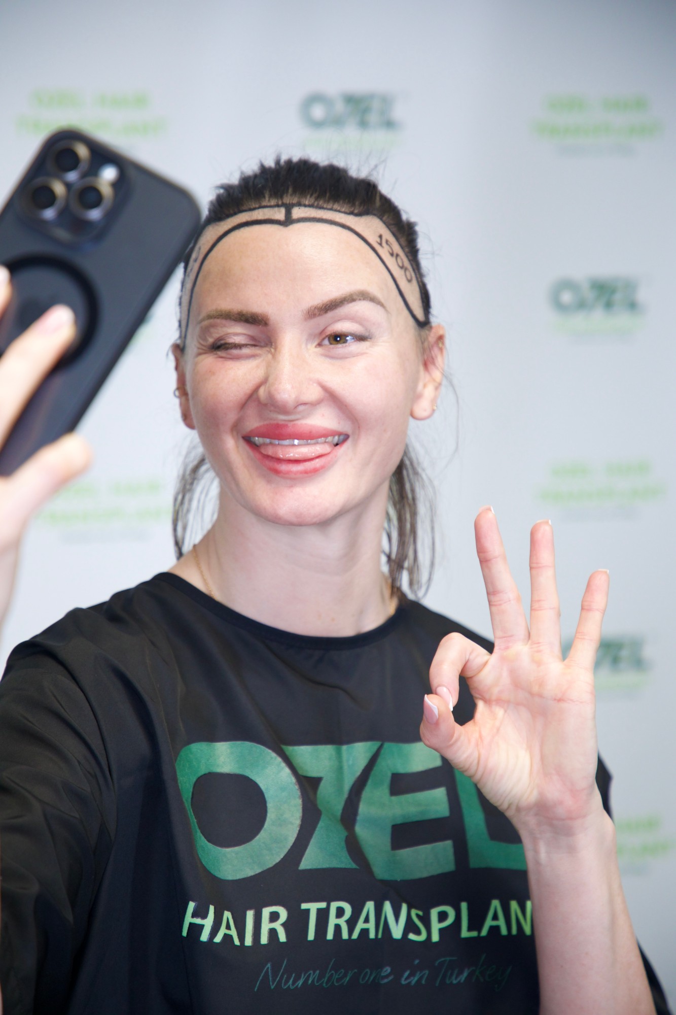 An OZEL client winking and making the OK sign while taking a selfie