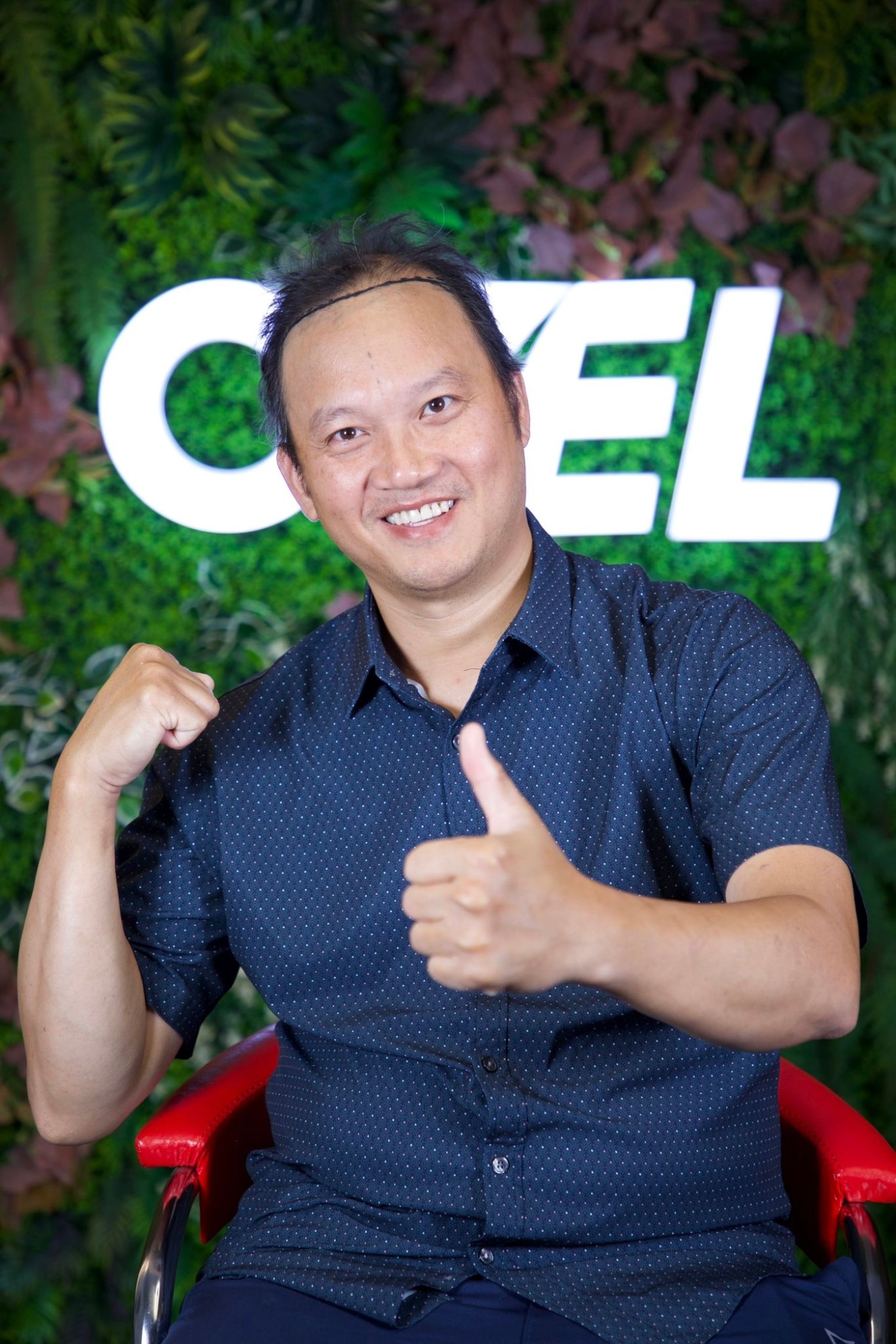 A smiling OZEL client giving a thumbs up in front of the OZEL sign